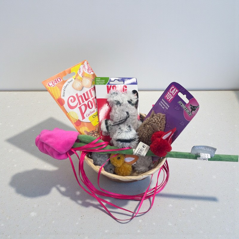 Korb mit Katzenspielzeug und Leckerlis, darunter Plüschtiere und Snacks in bunter Verpackung. Ein Osterkorb für Katzen.