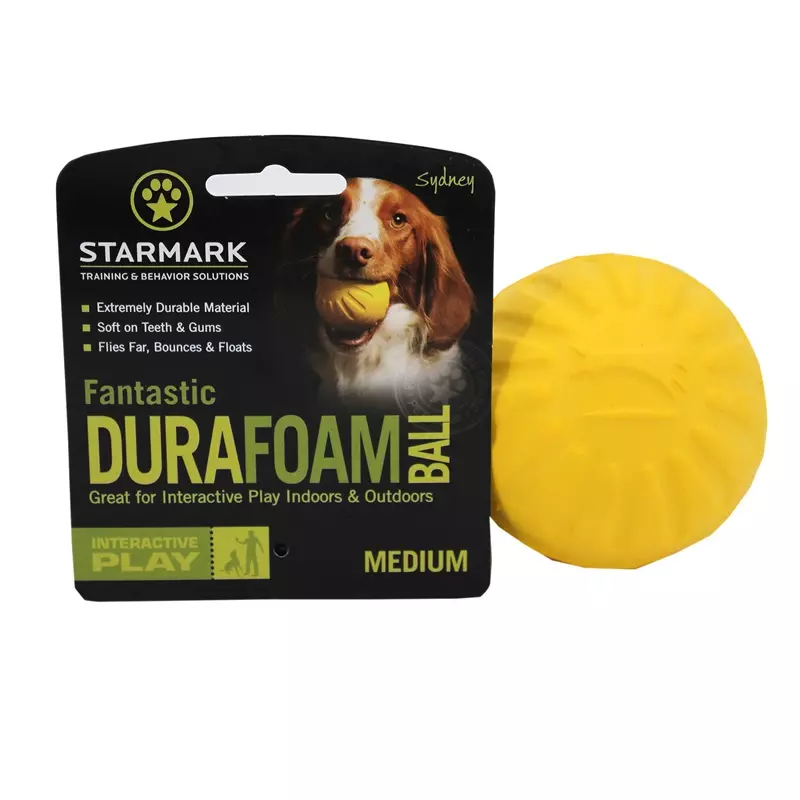 Jaune Starmark Fantastic Foam Ball pour chiens à côté de l'emballage du produit, avec un chien qui tient une balle dans sa gueule.