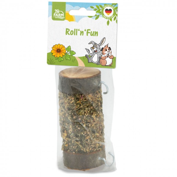 Cylindrical nibbling toy for small pets: wooden stick with dried herbs and seeds, in transparent plastic packaging. The cardboard header features ‘Roll’n’Fun’, the JR Farm logo and illustrations of a rabbit and a guinea pig.