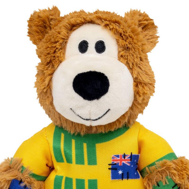 Brauner Plüschbär von der Brust aufwärts, flauschiges Fell, weiße Schnauze, schwarze Augen, lächelnder gestickter Mund. Er trägt ein gelbes T-Shirt mit grünen Streifen und einem aufgestickten australischen Flaggenpatch.