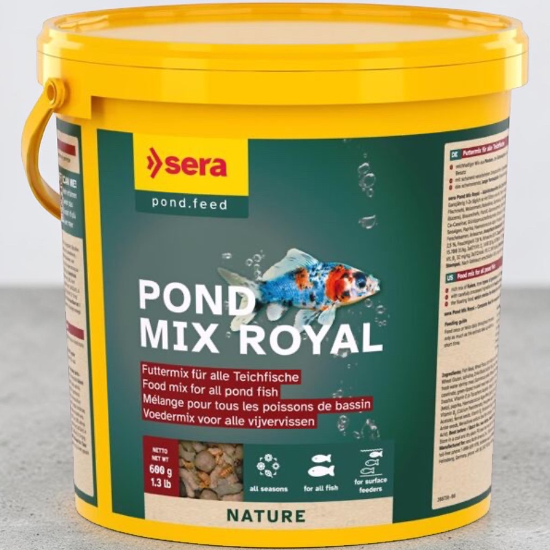 Seau jaune avec nourriture pour poissons de bassin « Pond Mix Royal Nature » de Sera. Étiquette vert foncé avec poisson tacheté et mention « POND MIX ROYAL ». Fenêtre transparente au fond montrant flocons, granulés et gammarus.