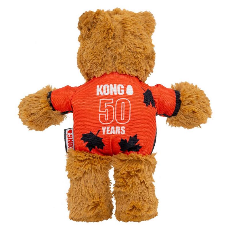 Flauschiger brauner Teddybär als Hundespielzeug, von hinten, mit orangefarbenem T-Shirt. Darauf in Weiß „KONG 50 YEARS“ und schwarze Blätter. Kleines KONG-Etikett seitlich. Vor weißem Hintergrund.