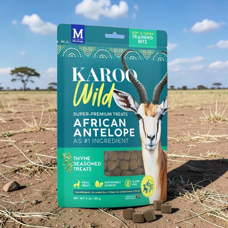 Montego Biscotti per cani Karoo Wild (antilope) in un packaging in piedi su un terreno di savana; davanti, biscotti cubici scuri. Background: prateria, cielo blu, alberi sparsi.