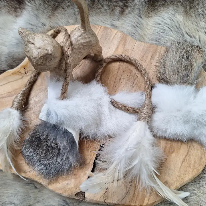 Holzbrett mit Katzenspielzeug aus Stoff, Federn und Jute. Zwei Katzenfiguren stehen auf dem Brett.