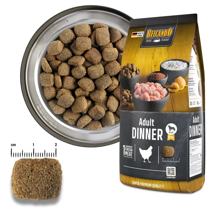 Cibo secco Belcando di colore marrone per cani adulti in una ciotola argentata, accanto alla confezione «Adult Dinner» dai colori oro e nero. Crocchette di dimensioni maggiori, circa 1,5 cm. Immagine: pollame fresco, patate, farina di semi d'uva.