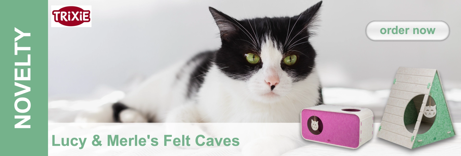 A black-and-white cat with bright green eyes lies relaxed. In the foreground are two felt cat caves: a pink, rectangular one with two openings and a beige-green, triangular one with a round entrance, both decorated with a cat’s face.