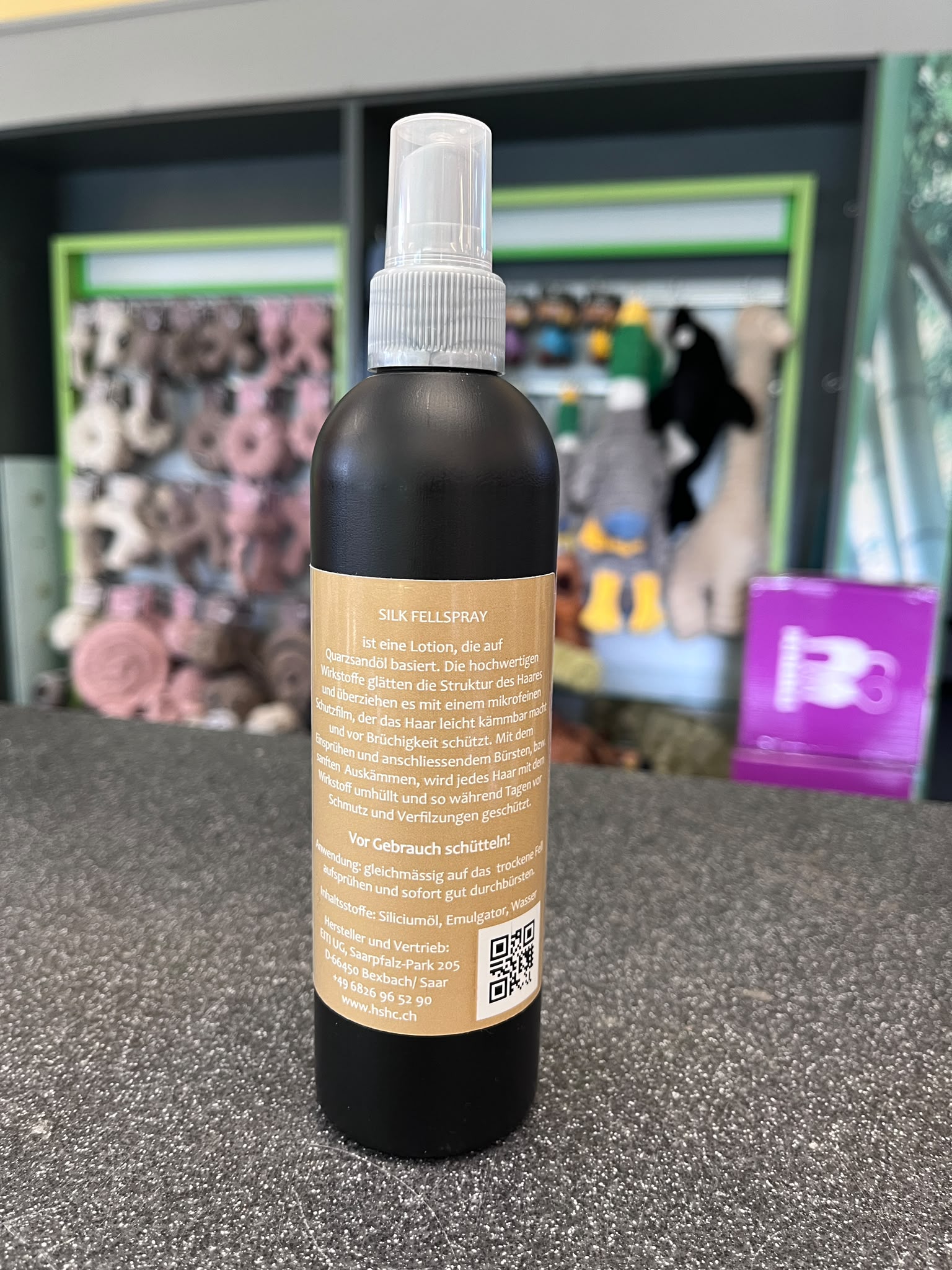 Spray pelage de haute qualité, marron foncé, pour chiens, avec buse blanche sur surface grise légèrement pailletée. Étiquette beige : protège de la saleté et des nœuds, apporte brillance. Flou : autres soins animaux.