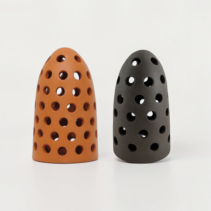 Orange und dunkle Keramik-Windlichter mit Lochmuster, kegelförmig.
