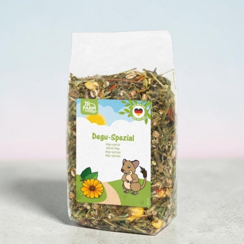 Sachet transparent « JR Farm » : aliment spécial pour dégus composé d'herbes vertes, de foin, de flocons de maïs jaunes et d'autres ingrédients séchés. Étiquette : dégus souriant, fleur jaune, ciel ensoleillé avec des nuages et logo.