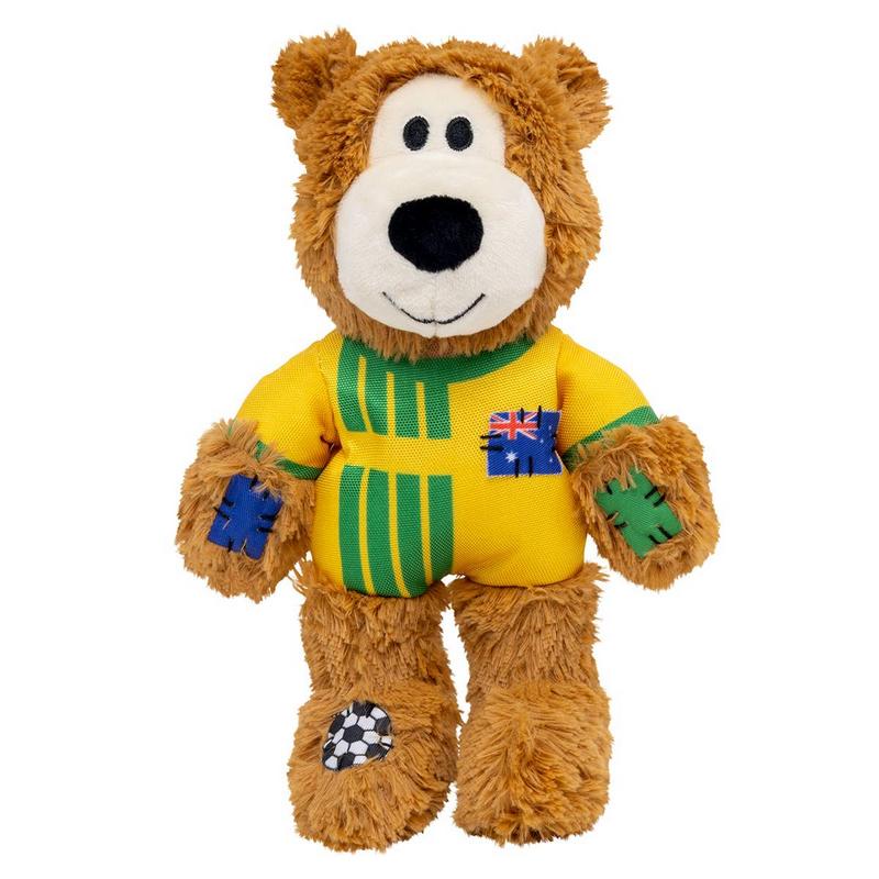 Flauschiger brauner Teddybär im gelben Trikot mit grünen Streifen steht aufrecht. Auf der Brust eine kleine australische Flagge, an den Armen blaue und grüne Flicken. Am linken Fuß ein schwarz-weißer Fußball-Aufnäher.