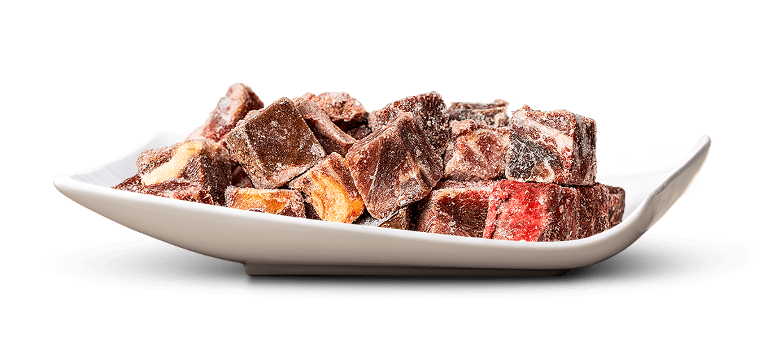 Gefrorene, würfelförmige Fleischstücke liegen auf einer weißen, rechteckigen Schale. Die Stücke zeigen verschiedene Rot- und Brauntöne, teils mit weißlicher Eisschicht überzogen, was ihren gefrorenen Zustand zeigt.
