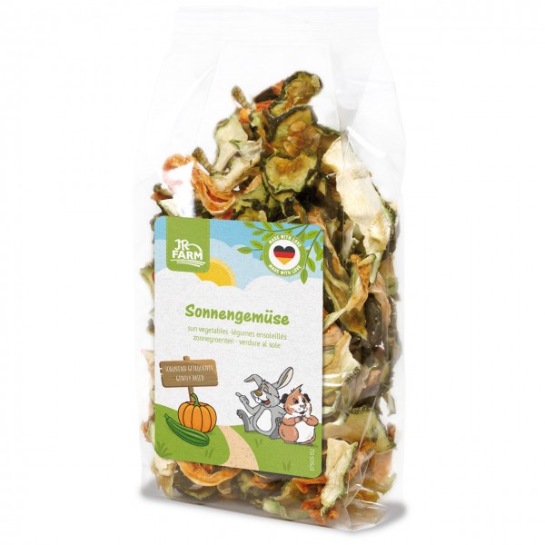 Transparent plastic bag containing dried vegetable slices (courgette, carrots) for animal feed. Label: ‘JR Farm Sun-Dried Vegetables’ featuring a cartoon rabbit and guinea pig, a pumpkin and a courgette in a meadow under the sun.