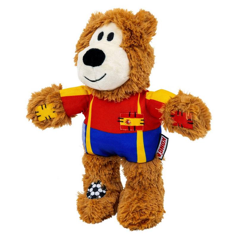 Orsacchiotto di peluche marrone con maglietta rossa con maniche gialle, pantaloni blu e bretelle gialle. Toppe con la bandiera della Spagna sul petto e con un pallone da calcio sul piede. Zona della bocca bianca, naso nero, sorriso.