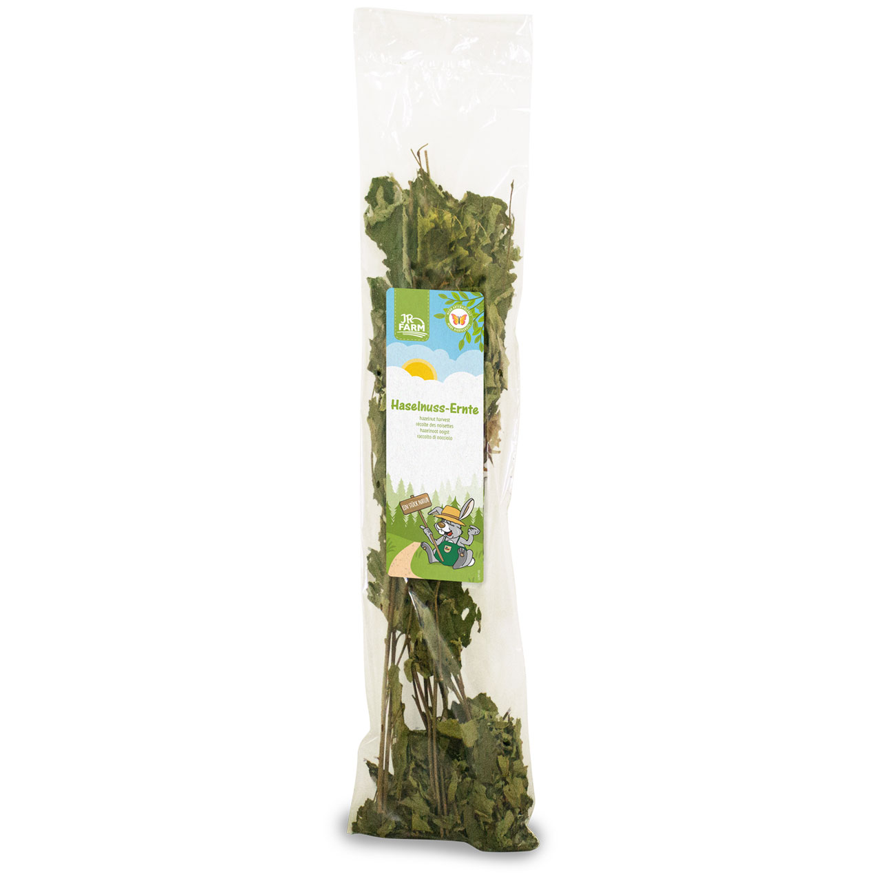 Transparent plastic packaging with dried hazelnut leaves and thin twigs. Colourful label with JR Farm logo, a sun and the name ‘Hazelnut Harvest’. Cartoon rabbit in farm attire. Leaves are dark green with a slight brown tinge.