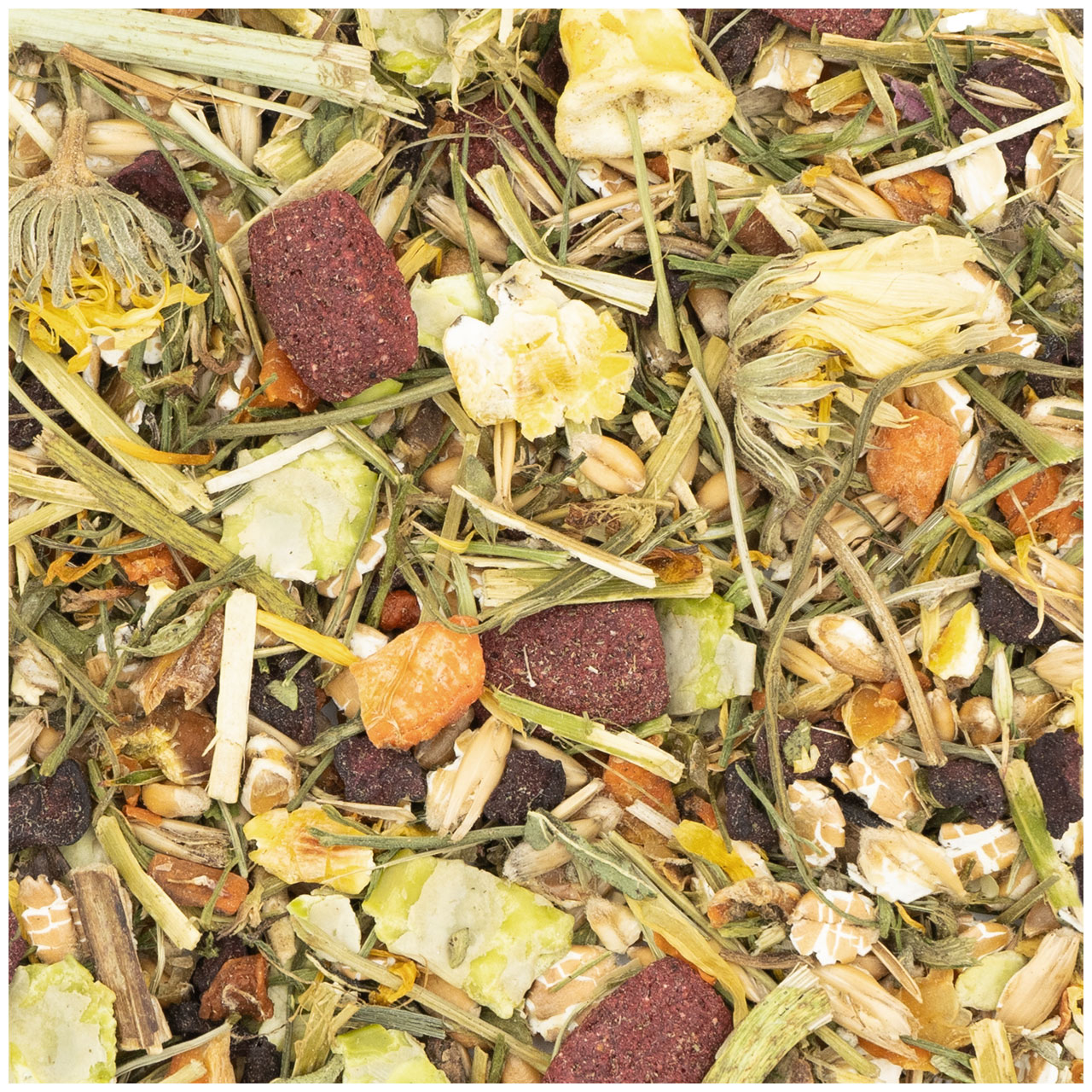 A detailed close-up of a natural feed mix consisting of dry green grasses, yellow petals such as marigolds, brown-red pellets, pieces of carrot, oat flakes, light green leaf fragments and dark berries.