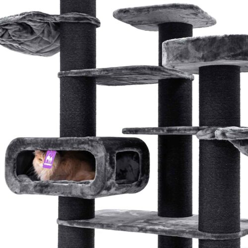 Grande tiragraffi a più livelli nei toni del grigio scuro e chiaro, con pali in sisal e piattaforme in peluche. Si vede una cuccia per gatti grigio chiaro, nella quale giace un gatto morbido e marrone chiaro con un'etichetta viola al collo.