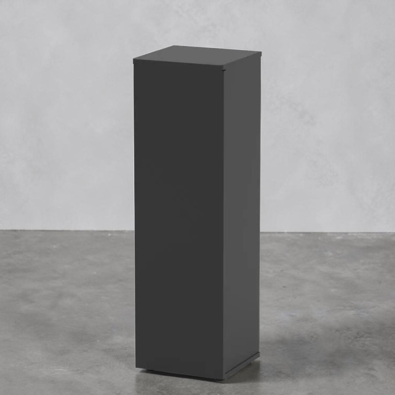 Ein hochaufragender, dunkelgrauer, rechteckiger Präsentationsständer steht vertikal auf Betonboden. Die matte, unstrukturierte Oberfläche zeigt leichte Schatten, die die Kanten betonen. Vor schlichtem, hellgrauen Hintergrund.