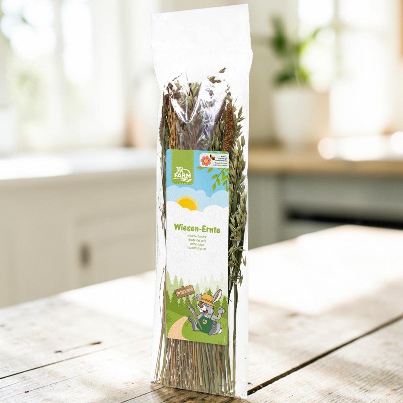 JR Farm ’s ‘Meadow Harvest’ in transparent plastic packaging on a rustic wooden table, filled with dried grasses and herbs. The label shows a rabbit wearing a hat and the words ‘Meadow Harvest’. A bright, out-of-focus kitchen in the background.