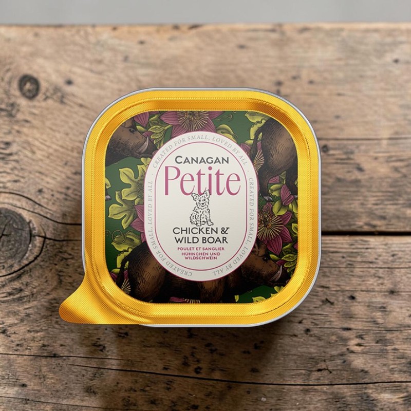 Boîte « Canagan » dorée, format «Petite» : pâtée «Poulet & Sanglier» pour petits chiens. Étiquette verte avec des sangliers et des fleurs violettes, logo représentant un chien. Pâté sans céréales présenté sur un support en bois.