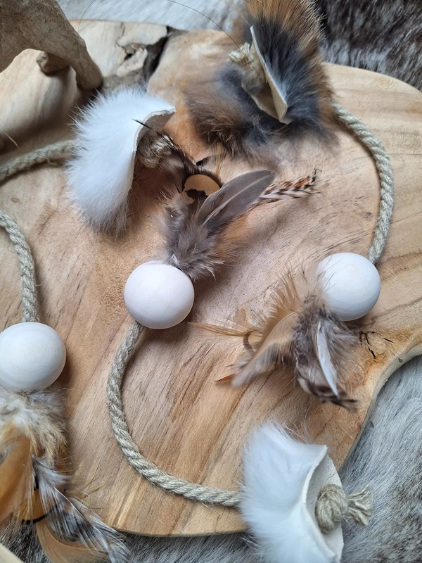 Handgemachtes Katzenspielzeug: Kugeln, Federn, Fell und Seil auf einer Holzscheibe.