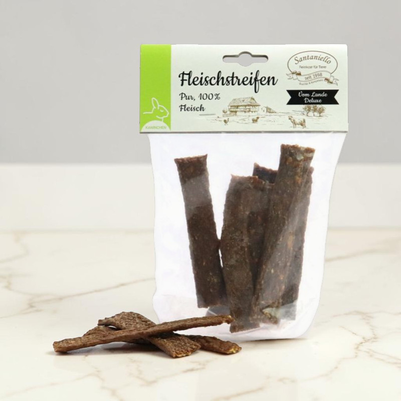 Durchsichtige Tüte mit mehreren dunklen, rechteckigen Kaninchen-Fleischstreifen für Hunde. Davor liegen einige getrocknete Hundesnacks auf heller Marmorfläche. Grünes Etikett: „Fleischstreifen Pur, 100% Fleisch Kaninchen“.
