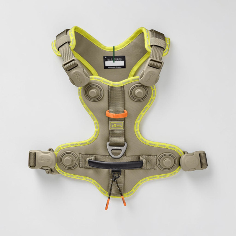Grey-green, ergonomic dog harness with reflective light yellow piping. Adjustable straps and buckles, Y-shaped chest pad, padded back panel, black handle and D-ring for the lead. ‘ Hunter ’ logos on the buckles.