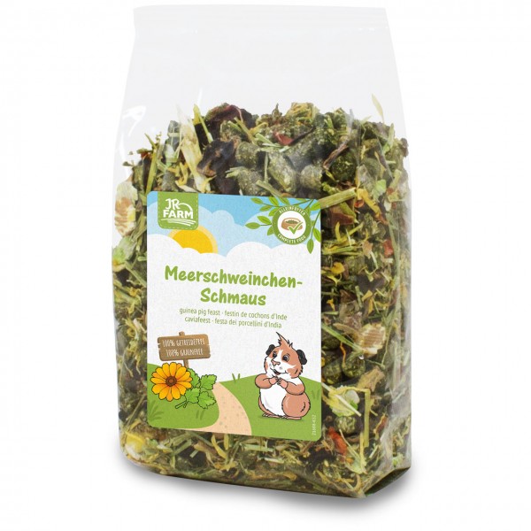 Transparente Plastiktüte mit JR FARM Meerschweinchen-Schmaus, trockenes Futter aus grünen Kräutern, Blättern und Gemüsestücken. Etikett: lachendes Cartoon-Meerschweinchen, orange Blume, Text „100% Naturtreue 100% Getreidefrei“.