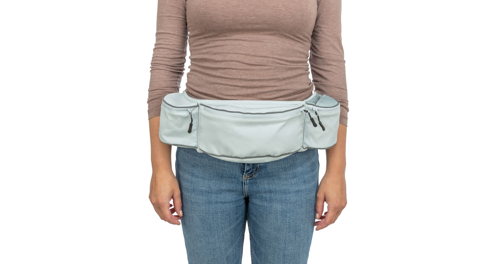 Eine Person trägt eine hellblaue Hüfttasche mit mehreren Reißverschlussfächern und reflektierendem Streifen um die Taille. Sie trägt ein braunes Langarmshirt und blaue Jeans. Die Tasche ist vorn sichtbar und gut gefüllt.