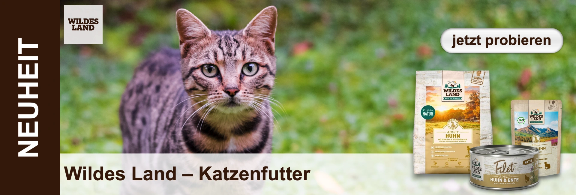 Getigerte Katze mit grünen Augen blickt frontal vor grünem Hintergrund. Rechts verschiedene Wildes Land Katzenfutterprodukte (Trocken- und Nassfutter). Links "NEUHEIT", oben rechts Button "jetzt probieren". Unten "Wildes Land – Katzenfutter".