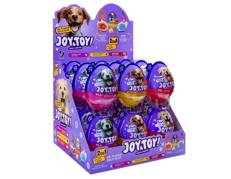Lila Verkaufsdisplay mit Joy & Toy! 2-in-1 Snack-Überraschungseier für Hunde. Lila, gelbe und pinke Eier mit lachenden Hunden, je mit Snack und Spielzeug. Oben ein brauner Hund, daneben Futter und blauer Gummiball.