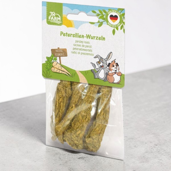 Confezione in plastica trasparente con radici di prezzemolo essiccate per roditori della linea "JR Farm". Raffigura un paesaggio idilliaco con coniglio e porcellino d'India e la scritta "NATURAL VITAMIN C".