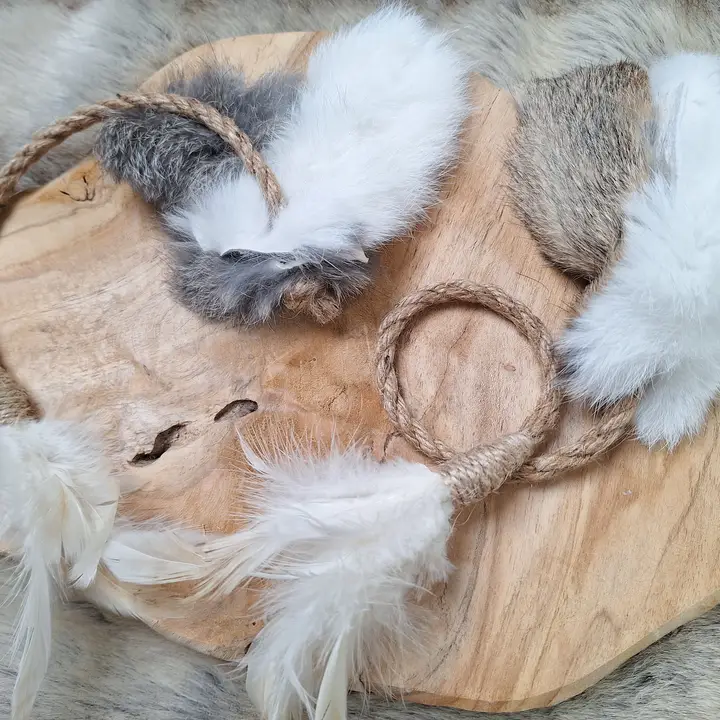 Verschiedene Katzenspielzeuge mit Federn, Fell und Sisalringen auf einer Holzscheibe.