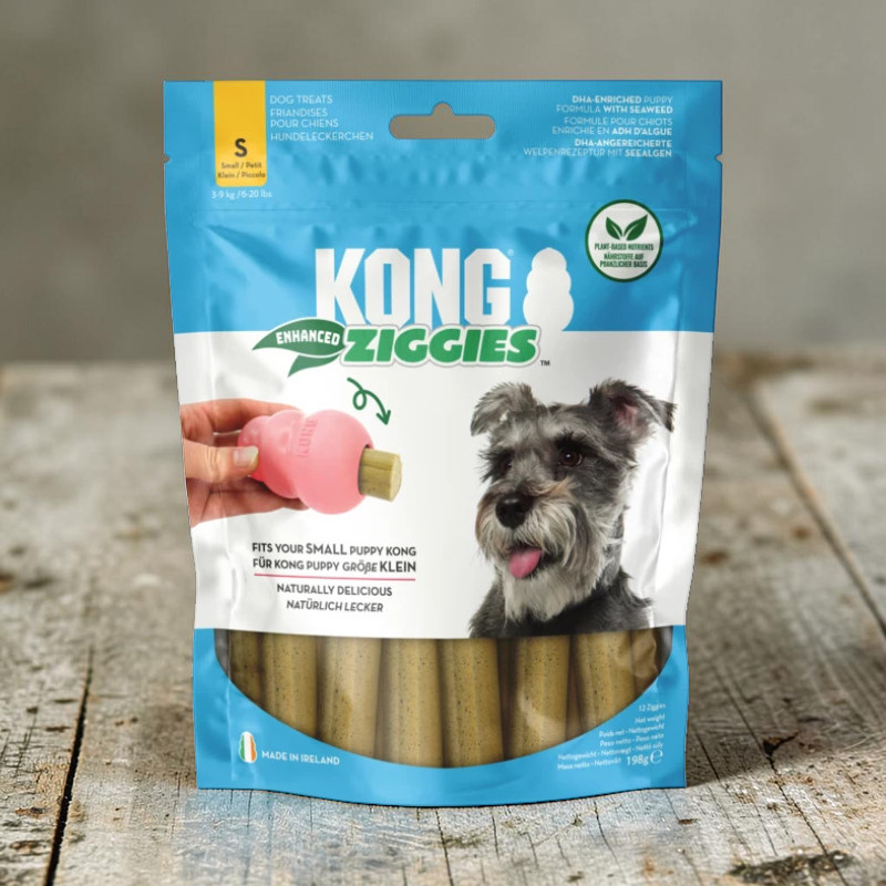 Hellblaue/weiße Verpackung von KONG Enhanced Ziggies Puppy. Oben rechts ein fröhlicher Welpe mit heraushängender Zunge. Links hält eine Hand ein pinkes KONG Puppy Spielzeug mit hellbraunem Ziggies-Stick.