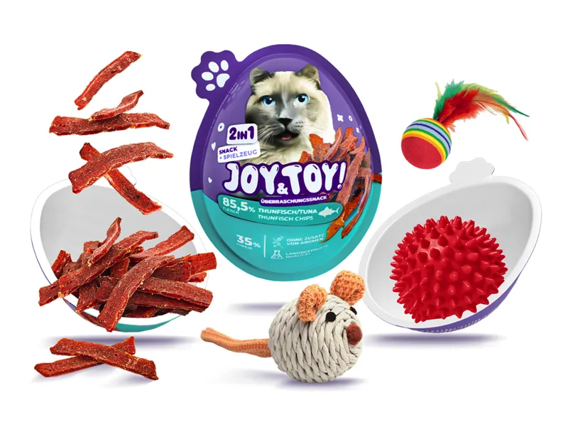 Katzenprodukte auf weißem Hintergrund: lila-türkise Eierpackung "JOY & TOY! Snack + Spielzeug" mit Katzenmotiv, Schale mit braunen Thunfisch-Snack-Streifen, Schale mit rotem stacheligem Spielball, Federball und gestrickte Spielzeugmaus.
