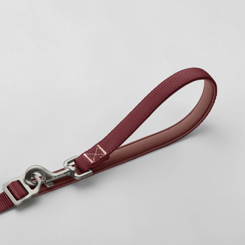 Gros plan sur une laisse pour chien rembourrée de couleur rouge baie. Poignée épaisse, mousqueton de sécurité robuste en aluminium argenté avec fermeture rapide et gravure « Hunter ».
