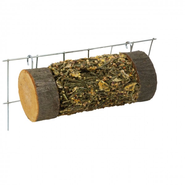 A cylindrical nibble log for pets, made from dried herbs, seeds and plant material. Both ends feature dark tree bark, giving it the appearance of a natural log. It hangs horizontally from a mesh wall using metal hooks.