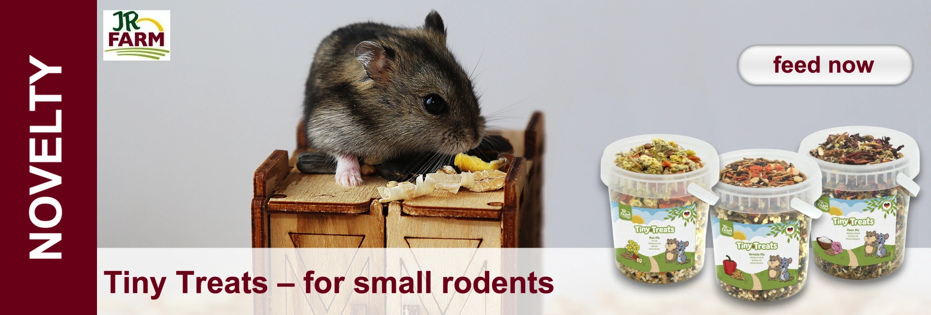 Small hamster eating on a miniature wooden chest of drawers, next to it three containers with rodent treats.
