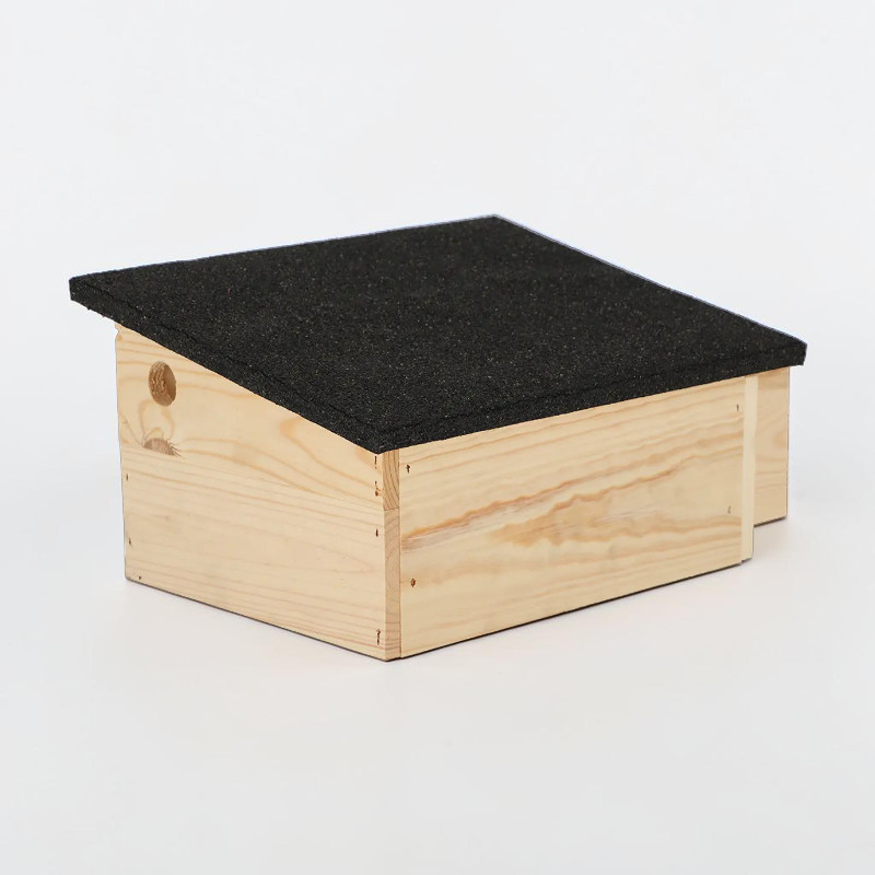 Abri rectangulaire pour hérissons en bois d'épicéa clair, avec toit en pente recouvert de bitume noir à gros grains pour évacuer l'eau de pluie. Allongé et doté d'une entrée discrète, il sert de refuge pour repos et hibernation.