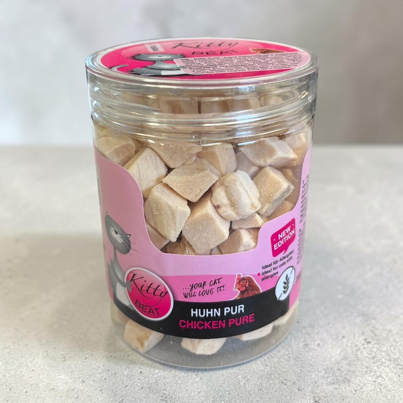 Transparent container containing light beige, square, freeze-dried chicken cubes for cats. Pink label: ‘Kitty Beat Pure Chicken’ featuring a cat. Ideal for cats with allergies, 100% chicken breast.