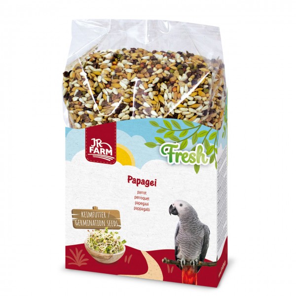 Eine transparente Verpackung mit Vogelfutter für Papageien, gefüllt mit verschiedenen Samen und Körnern. Auf dem weißen Etikett sind das "JR FARM" Logo, "Fresh", "Papagei", eine Schale Keimfutter und ein grauer Papagei auf einem Ast zu sehen.