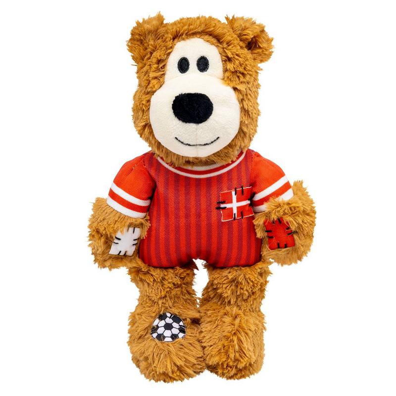 Orsacchiotto marrone con maglia da calcio a strisce rosse e bianche con toppe a forma di croce; sul piede una toppa a forma di pallone da calcio. In piedi, sorridente.