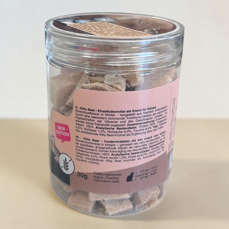 Barquette plastique transparente avec cubes de magret de canard lyophilisé marron clair, friandises pour chats. Étiquette rose : « NEW EDITION », « 30 g », « Kitty Beat Canard Pur » + symbole « sans gluten ».