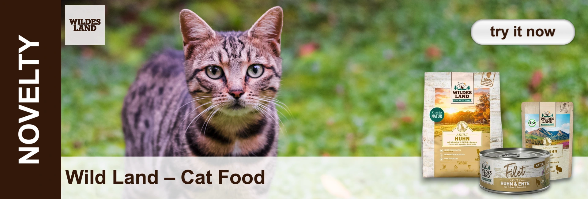 A tabby cat with green eyes looks into the camera, half-hidden in grass. Background: blurred green and reddish plants. Beside it, ‘Wildes Land’ cat food: a ‘Chicken Adult’ bag and a ‘Chicken & Duck’ tin. Logo at top.