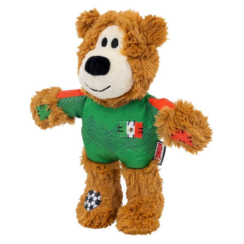 Orsacchiotto di peluche marrone e soffice con maglia verde a zig-zag. Sul petto toppa con bandiera messicana, maniche a strisce arancioni e rosse. Sul piede destro piccola toppa a pallone da calcio. Faccia marrone chiaro, occhi neri, naso e sorriso.