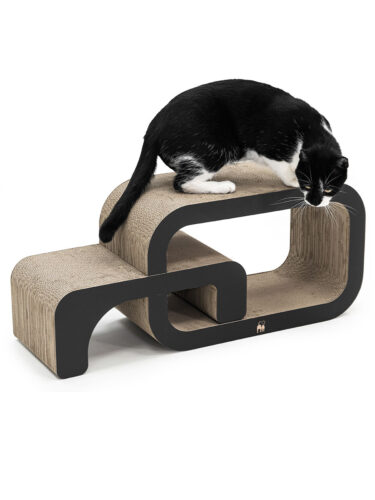 Gatto bianco e nero su un moderno tiragraffi in cartone ondulato con bordi neri. Ha zampe e macchie sul muso bianche, è proteso in avanti sul piano superiore e guarda verso il basso. Forma sinuosa, più livelli.