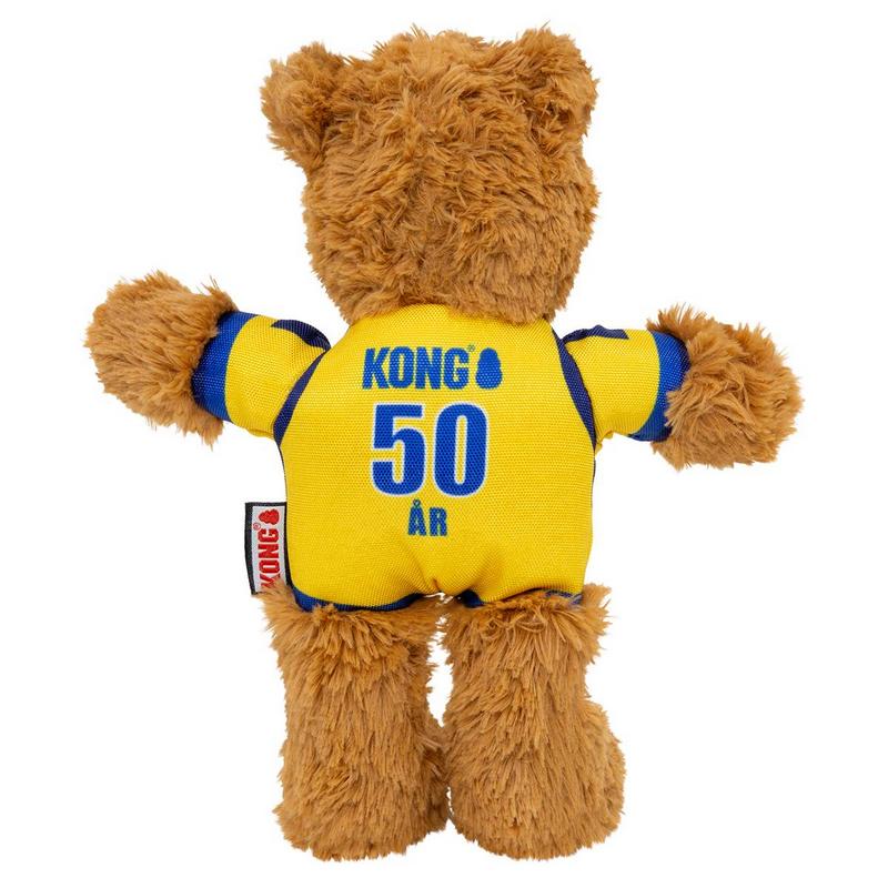 Orsacchiotto di peluche marrone visto da dietro, con maglietta gialla e dettagli blu. Sulla schiena in blu la scritta "Kong", il numero "50" grande e la parola "ÅR" per il 50° anniversario. Testa e arti visibili.