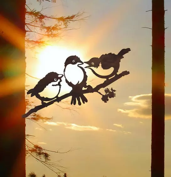Silhouettes of three chicks on a branch in front of an orange-coloured sky. Garden decoration.