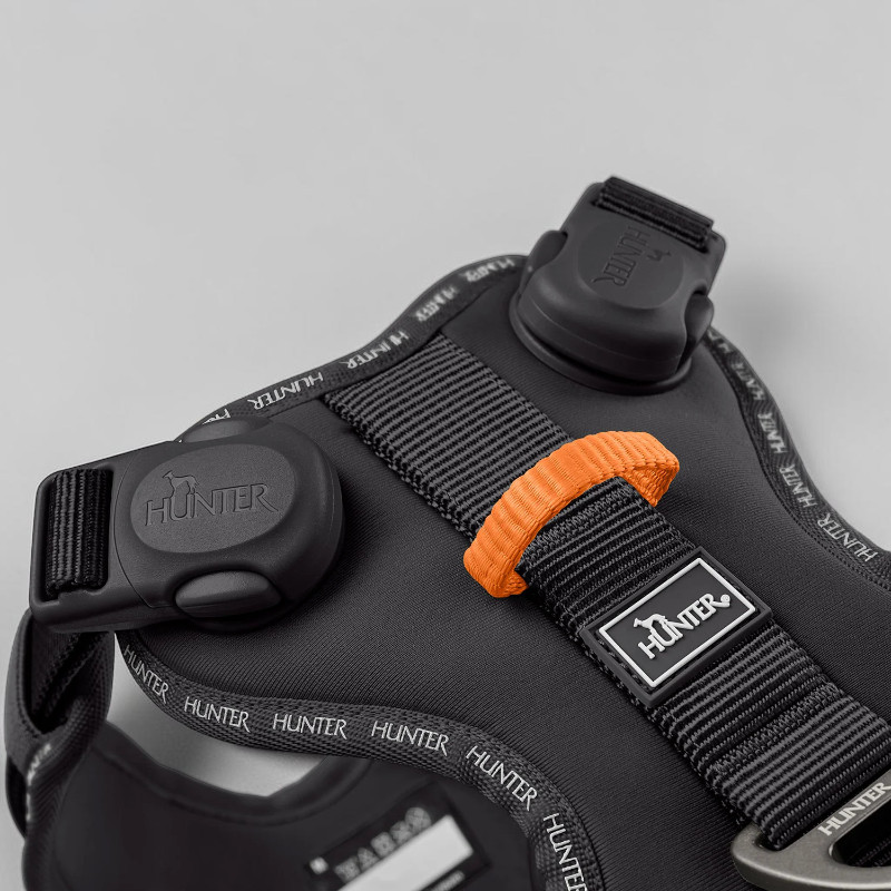 Close-up of the black ergonomic ErgoMove Pro dog harness with a padded back panel, wide adjustable straps, an orange loop and sturdy black magnetic buckles. Reflective Hunter lettering and an aluminium D-ring.