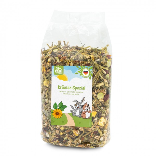 Transparent bag containing JR Farm Herbal Special pet food for rodents, filled with a natural blend of hay, dried herbs and other ingredients. Label: a landscape featuring a hare, a guinea pig and a yellow flower.