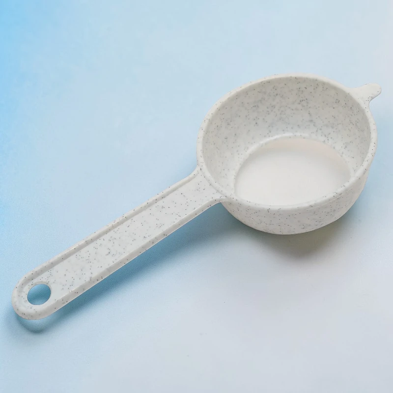 Nahaufnahme eines weißen, gesprenkelten Siebs aus Kunststoff mit Griff und Loch zum Aufhängen.